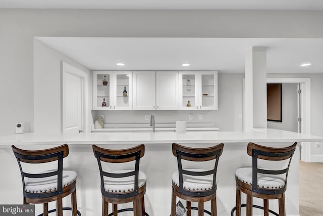 kitchen with light carpet, recessed lighting, white cabinets, light countertops, and glass insert cabinets