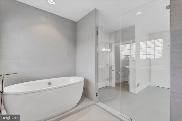 bathroom featuring a freestanding tub, toilet, a stall shower, tile walls, and tile patterned flooring