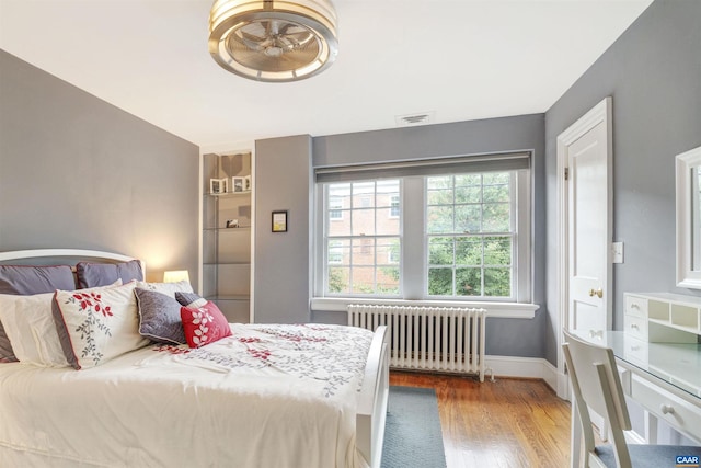 bedroom with radiator heating unit, wood finished floors, visible vents, and baseboards