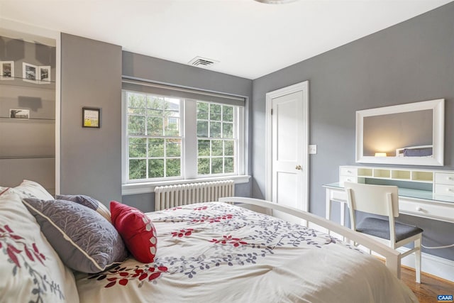 bedroom with visible vents, radiator, and wood finished floors