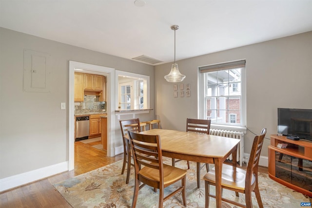 dining room featuring light wood finished floors, visible vents, radiator, baseboards, and electric panel