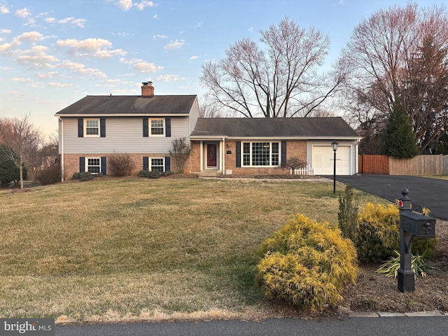 tri-level home with a front lawn, driveway, fence, a garage, and a chimney