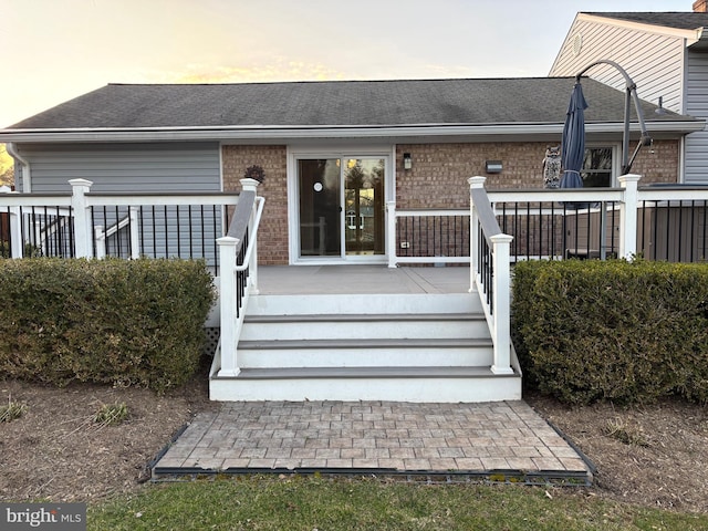 rear view of property featuring a shingled roof, brick siding, and a wooden deck