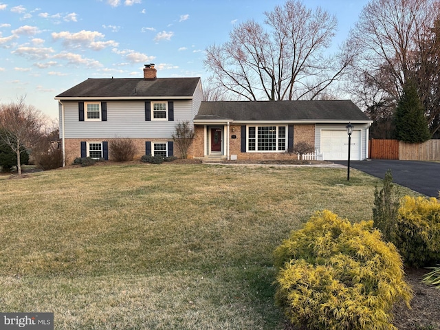 split level home featuring fence, aphalt driveway, a front yard, a chimney, and a garage