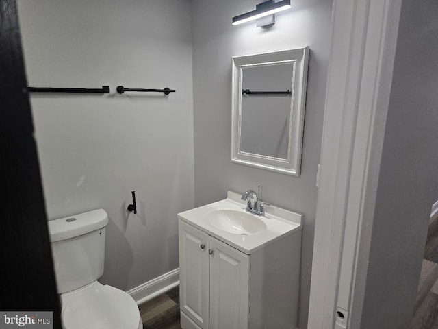 half bathroom with toilet, vanity, baseboards, and wood finished floors