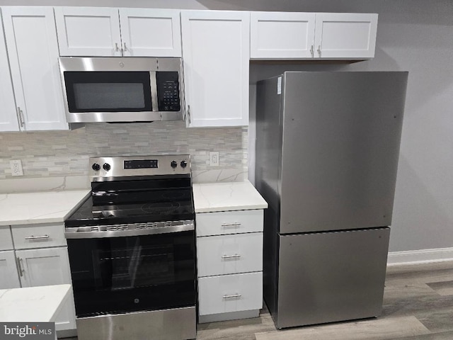 kitchen with light stone countertops, white cabinets, light wood-style floors, appliances with stainless steel finishes, and tasteful backsplash