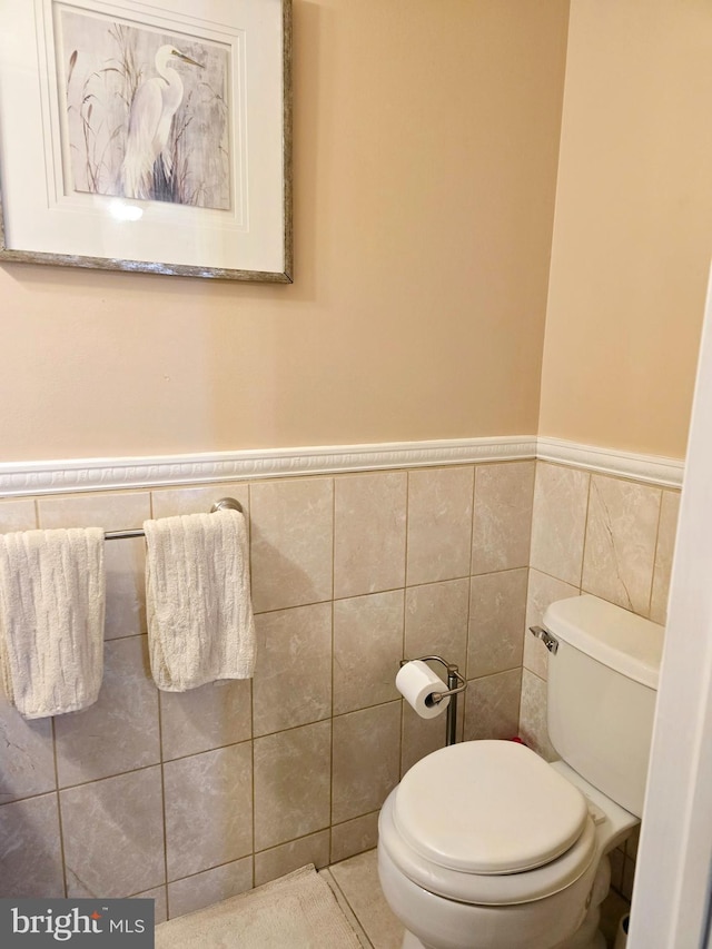 half bathroom with tile patterned flooring, tile walls, toilet, and a wainscoted wall