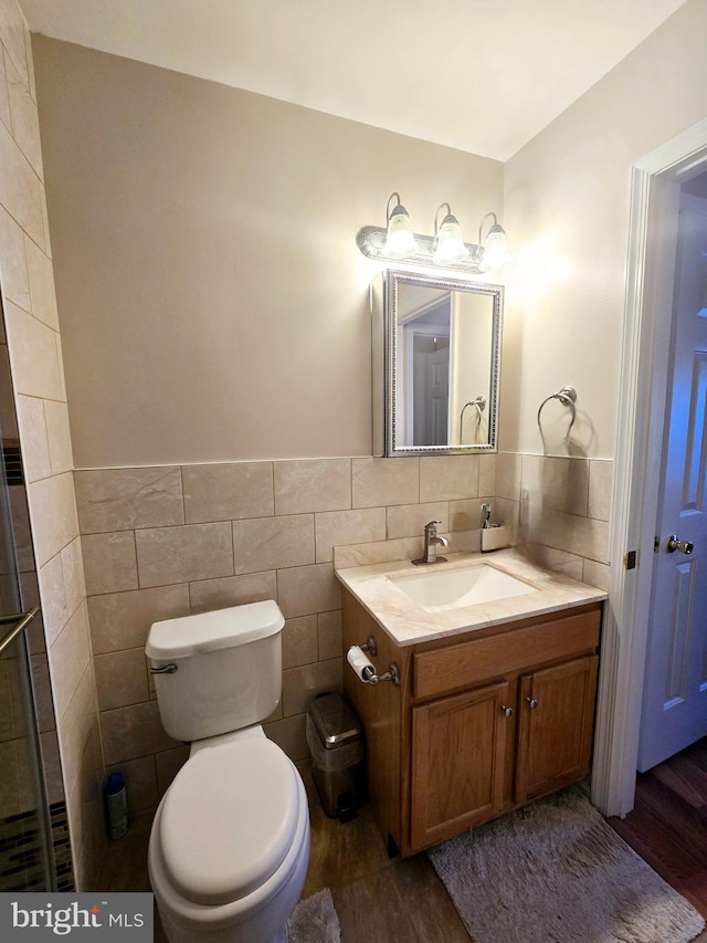 bathroom with a wainscoted wall, toilet, vanity, wood finished floors, and tile walls