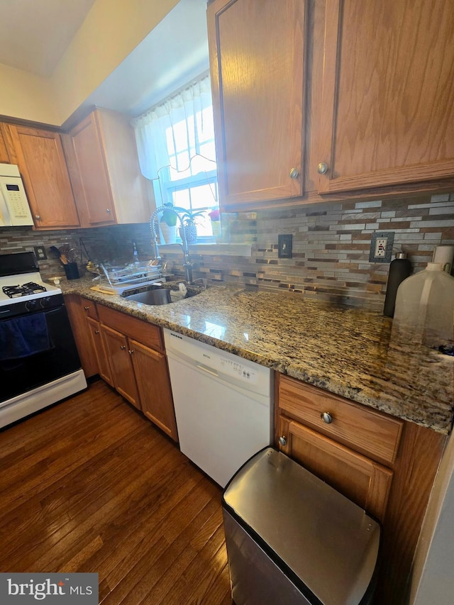 kitchen featuring white appliances, light stone counters, a sink, dark wood-type flooring, and backsplash