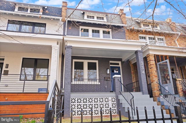 multi unit property featuring mansard roof, brick siding, and covered porch