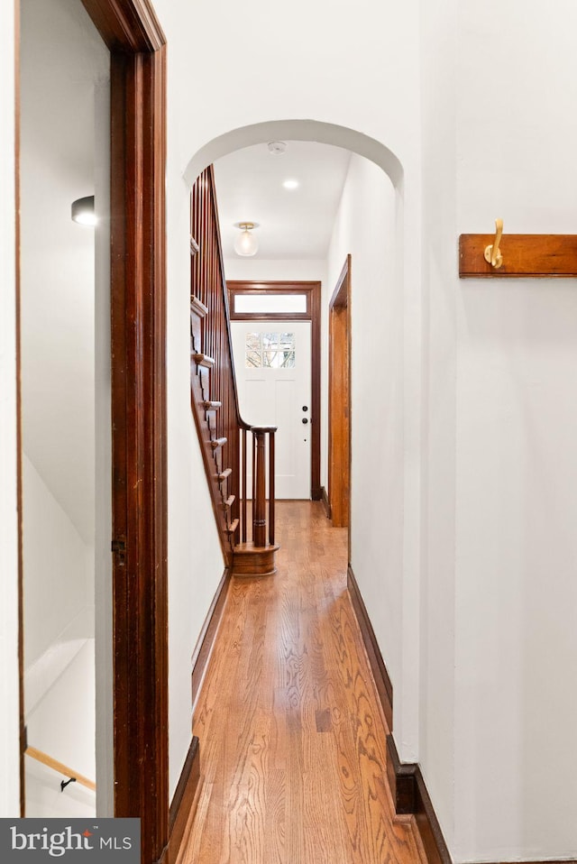 hallway with baseboards, arched walkways, light wood-style flooring, and stairs