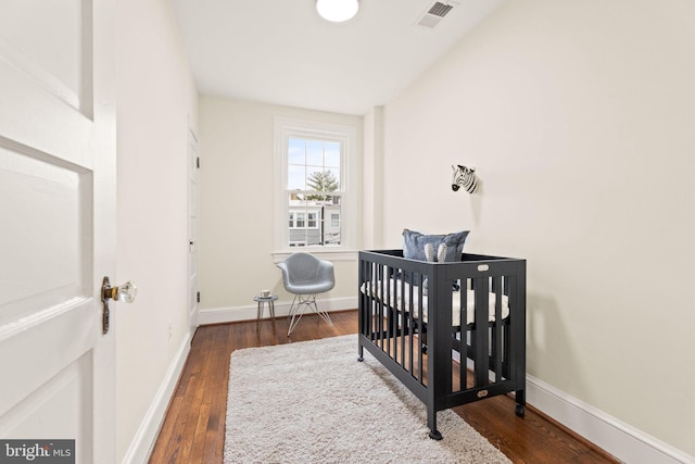 bedroom with a nursery area, baseboards, visible vents, and wood-type flooring