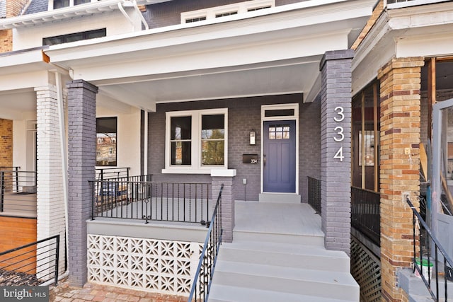 doorway to property with mansard roof, covered porch, and brick siding