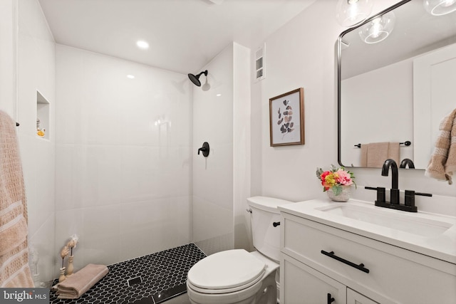 bathroom featuring a tile shower, visible vents, toilet, and vanity