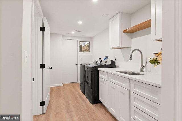 laundry room with light wood-type flooring, visible vents, a sink, washing machine and dryer, and cabinet space