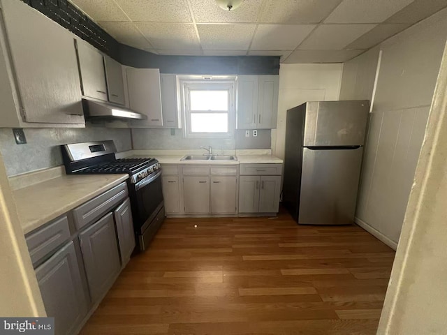 kitchen featuring light wood-type flooring, under cabinet range hood, a sink, appliances with stainless steel finishes, and light countertops