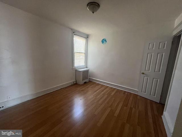 unfurnished bedroom featuring baseboards, radiator, and wood finished floors