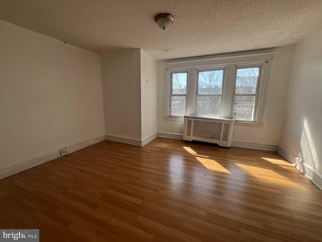 spare room with baseboards, a textured ceiling, wood finished floors, and radiator heating unit