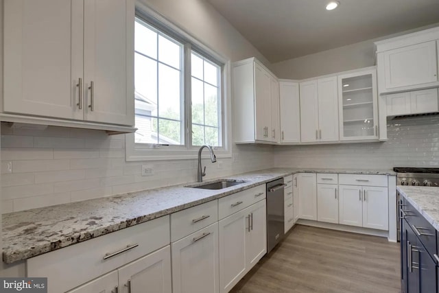 kitchen featuring light wood-type flooring, a sink, stainless steel dishwasher, white cabinetry, and glass insert cabinets