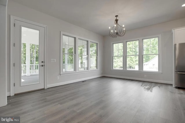 unfurnished dining area with wood finished floors, plenty of natural light, and a chandelier