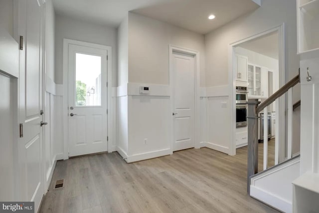 foyer entrance featuring recessed lighting, stairway, wainscoting, and light wood finished floors