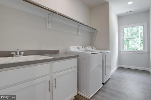 clothes washing area with visible vents, light wood-type flooring, washer and dryer, a sink, and cabinet space