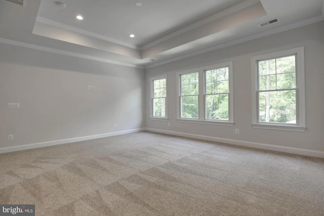 carpeted spare room featuring a tray ceiling, crown molding, baseboards, and visible vents