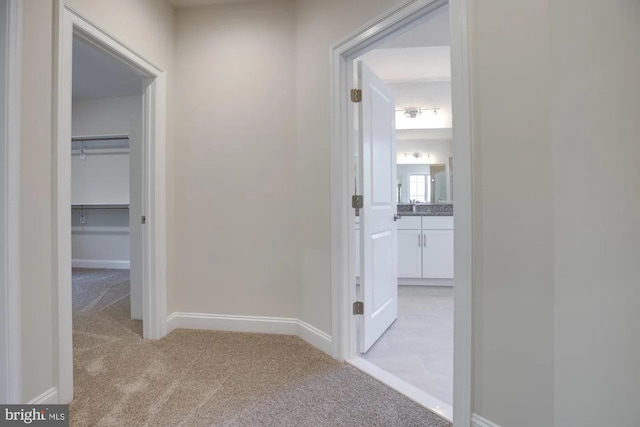 hallway featuring light colored carpet and baseboards