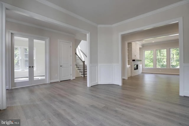 unfurnished living room with wood finished floors, stairway, french doors, and ornamental molding