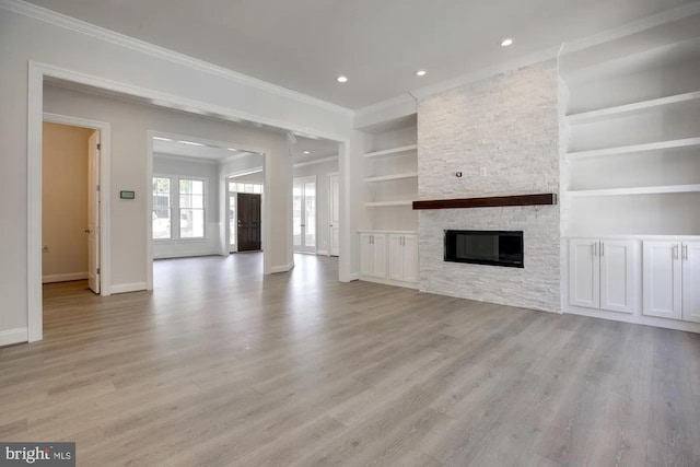 unfurnished living room featuring crown molding, baseboards, built in features, a stone fireplace, and light wood-style flooring