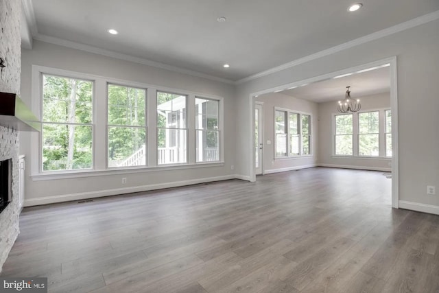 unfurnished living room with crown molding, a stone fireplace, recessed lighting, wood finished floors, and a notable chandelier