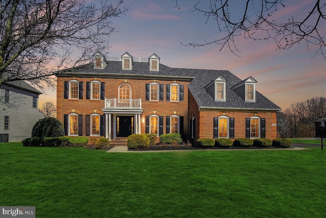 georgian-style home with a front yard, brick siding, and a balcony