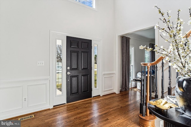 foyer entrance featuring visible vents, stairs, wainscoting, wood finished floors, and a decorative wall