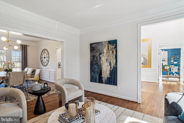 living room featuring a wainscoted wall, wood finished floors, an inviting chandelier, crown molding, and a decorative wall