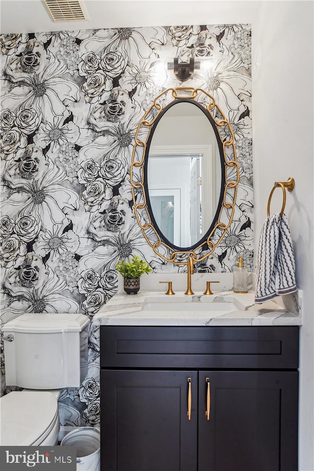 half bath featuring visible vents, toilet, and vanity