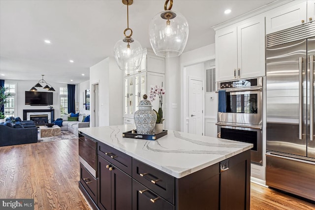 kitchen with a kitchen island, light wood-style flooring, stainless steel appliances, white cabinets, and a glass covered fireplace