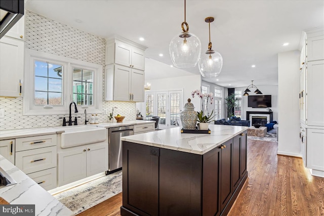 kitchen featuring light stone counters, a sink, white cabinets, stainless steel dishwasher, and open floor plan