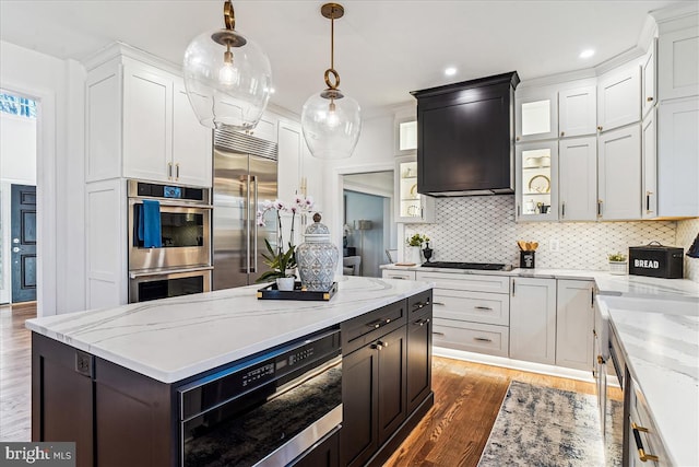 kitchen with decorative backsplash, wood finished floors, appliances with stainless steel finishes, and wall chimney exhaust hood