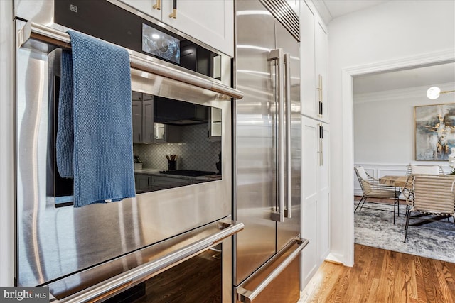 kitchen featuring stainless steel appliances, white cabinets, crown molding, light wood-type flooring, and backsplash