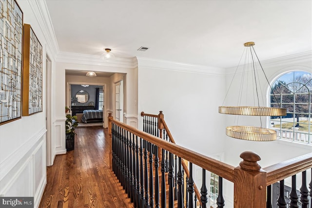 corridor with visible vents, an upstairs landing, ornamental molding, dark wood finished floors, and a decorative wall