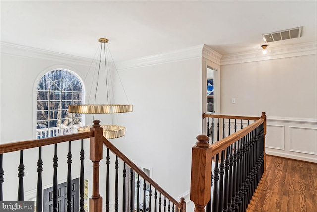 hallway with wood finished floors, an upstairs landing, visible vents, and ornamental molding