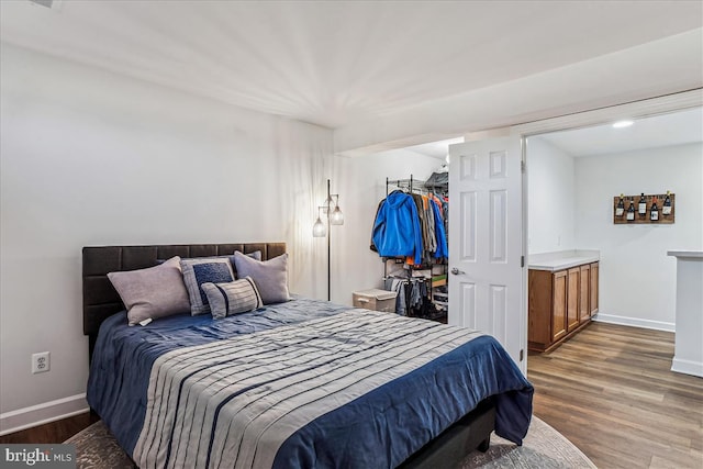 bedroom with a spacious closet, baseboards, and wood finished floors