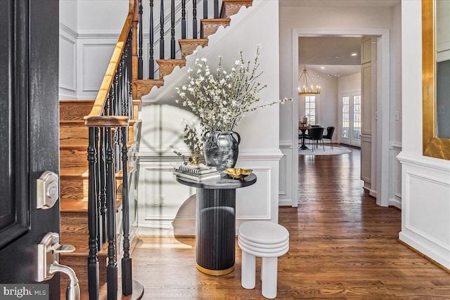 foyer with wood finished floors, a wainscoted wall, stairs, a decorative wall, and a chandelier