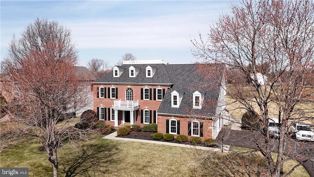 georgian-style home featuring brick siding, a front yard, and a balcony