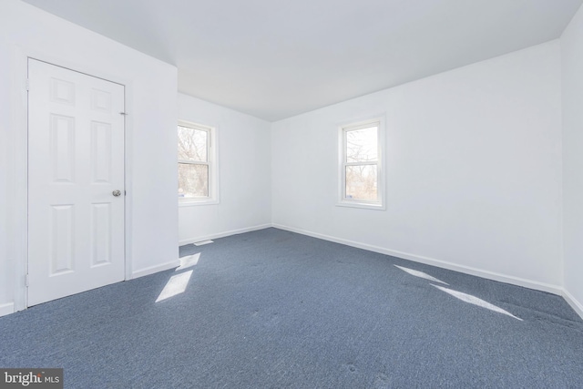 empty room with a wealth of natural light, baseboards, and dark carpet