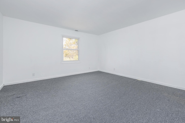 spare room with dark carpet and baseboards