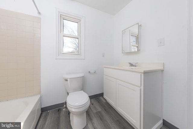 full bathroom with baseboards, toilet, vanity, wood finished floors, and washtub / shower combination