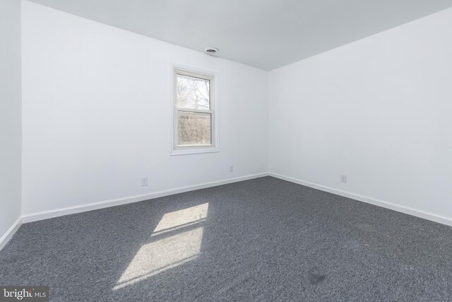 unfurnished room featuring visible vents, baseboards, and dark carpet