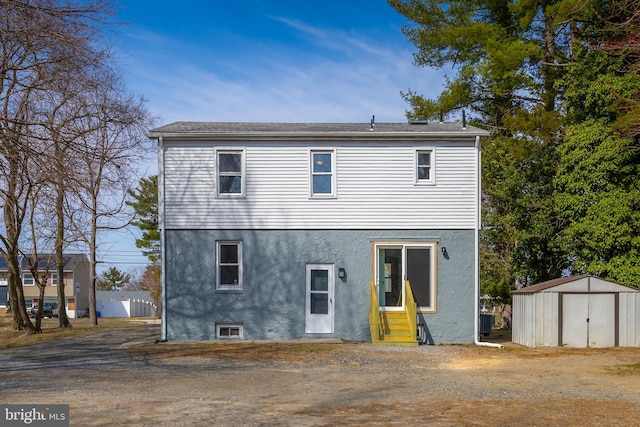 rear view of property featuring entry steps, an outbuilding, a shed, and stucco siding