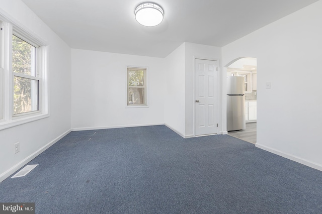 carpeted spare room featuring visible vents, baseboards, and arched walkways